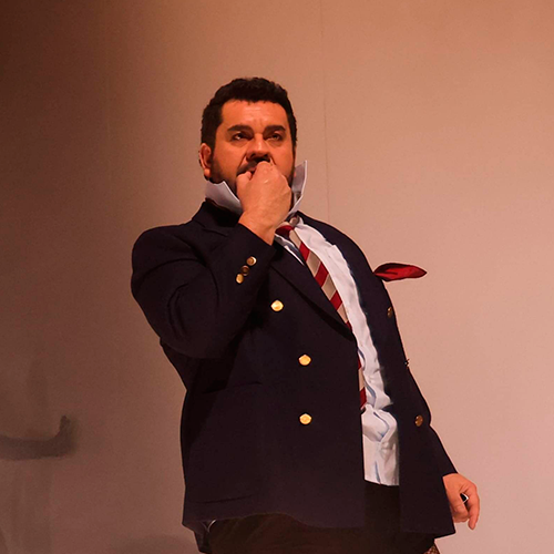 Luis in a navy uniform, covering his mouth as he performs in Ariadne auf Naxos.