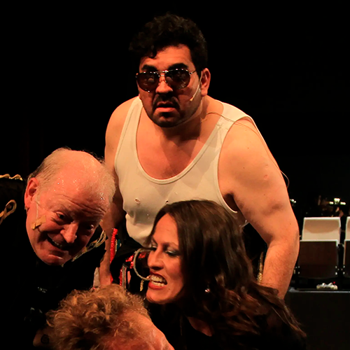 Luis in a white tank top, wearing sunglasses, on stage in Mahagonny.