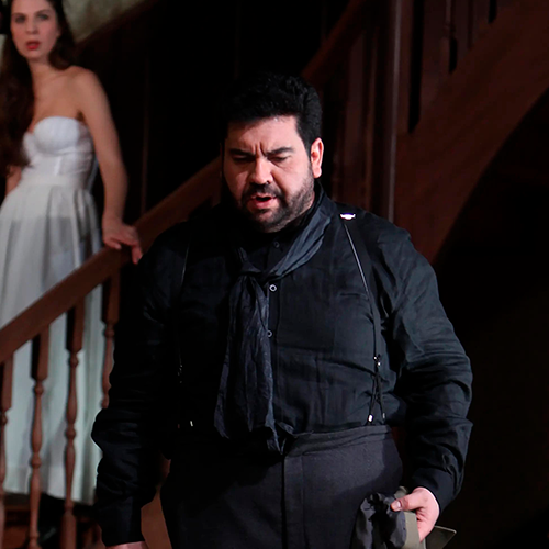 Luis walking down a staircase while a woman watches him in Carmen.