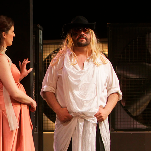 uis standing confidently in a white robe and hat in Cosi fan tutte.