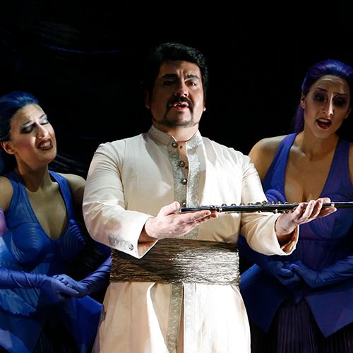 Luis holding a magic flute while singing, flanked by two women in Die Zauberflöte.